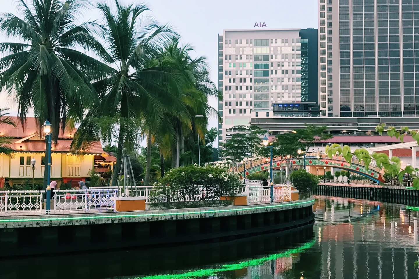 Traditional riverside house and palms at Kampung Morten with modern towers beyond