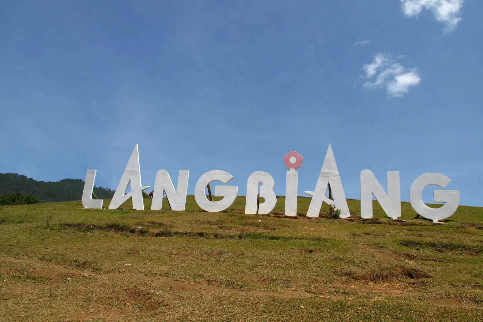 Large LANGBIANG sign on a grassy highland slope under blue sky
